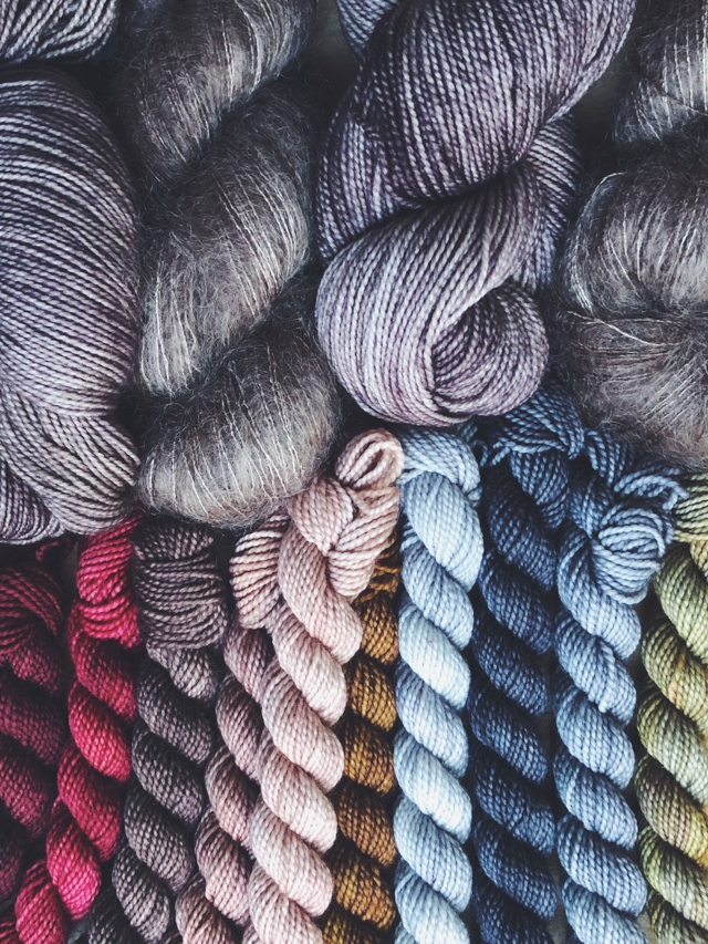 Image of a rainbow of mini skeins and soft gray main color yarn like clouds surrounding it.