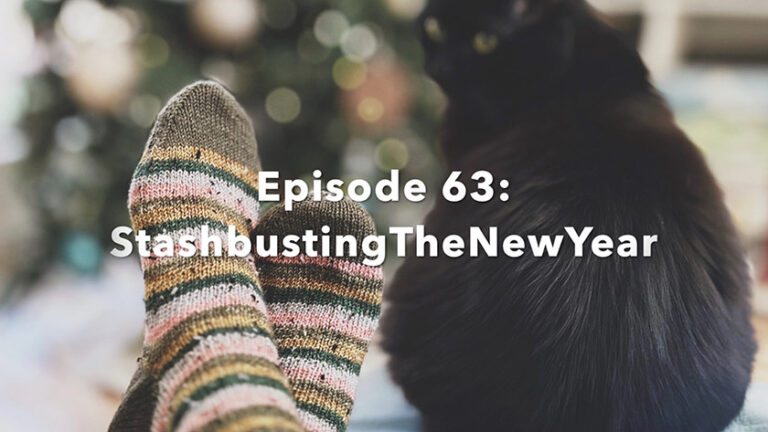 Image of hand knit socks next to a sometimes bad black cat, in front of the Christmas tree.