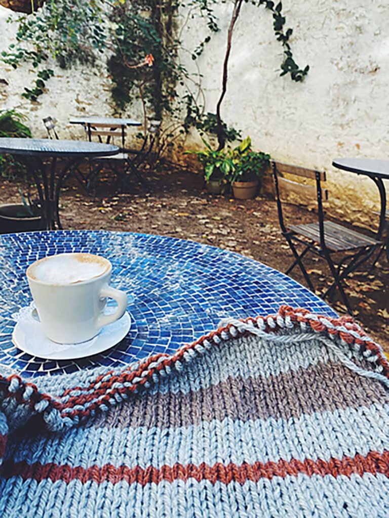 Image of my Easton sweater in process on a mosaic cafe table in central Texas with an almond milk cappucino.