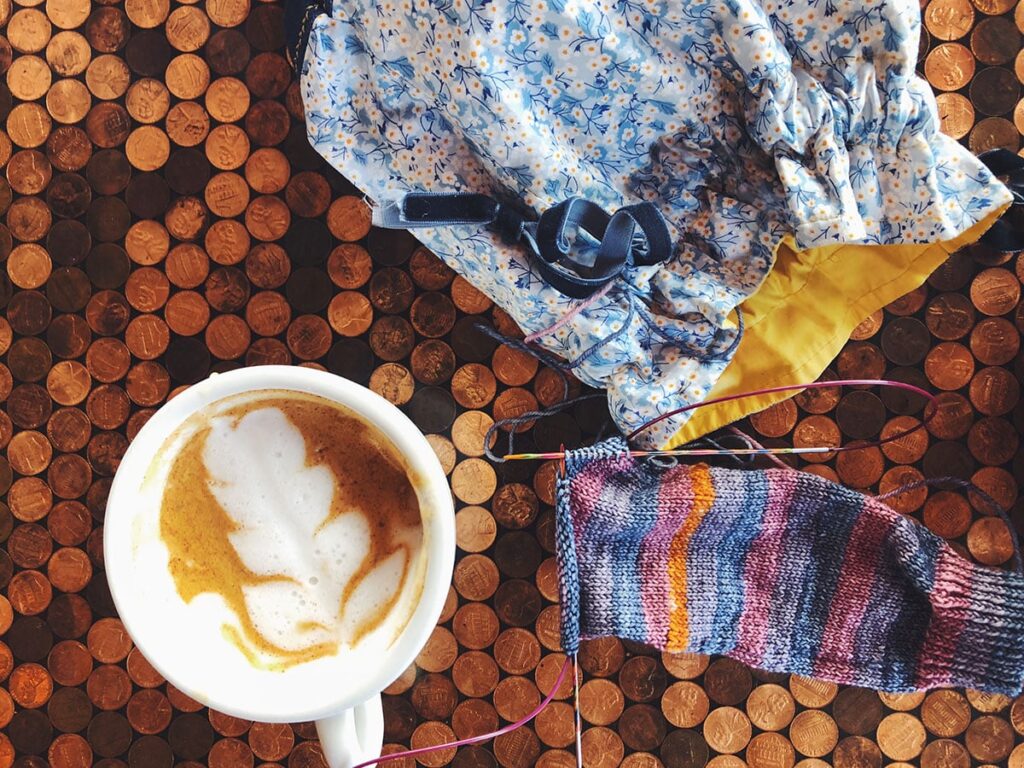 Image of my socks knit in the Michelle colorway in the perfect small travel size bag on a penny-tiled cafe table.