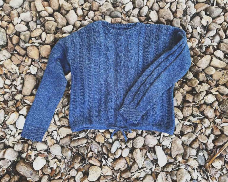 Image of my finished LAtely Pullover, a cabled worsted weight sweater with drawstring hem, laid on the ground.