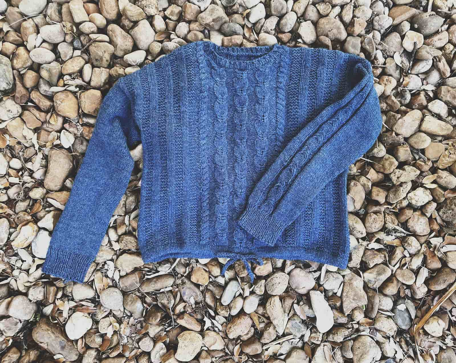 Image of my finished LAtely Pullover, a cabled worsted weight sweater with drawstring hem, laid on the ground.