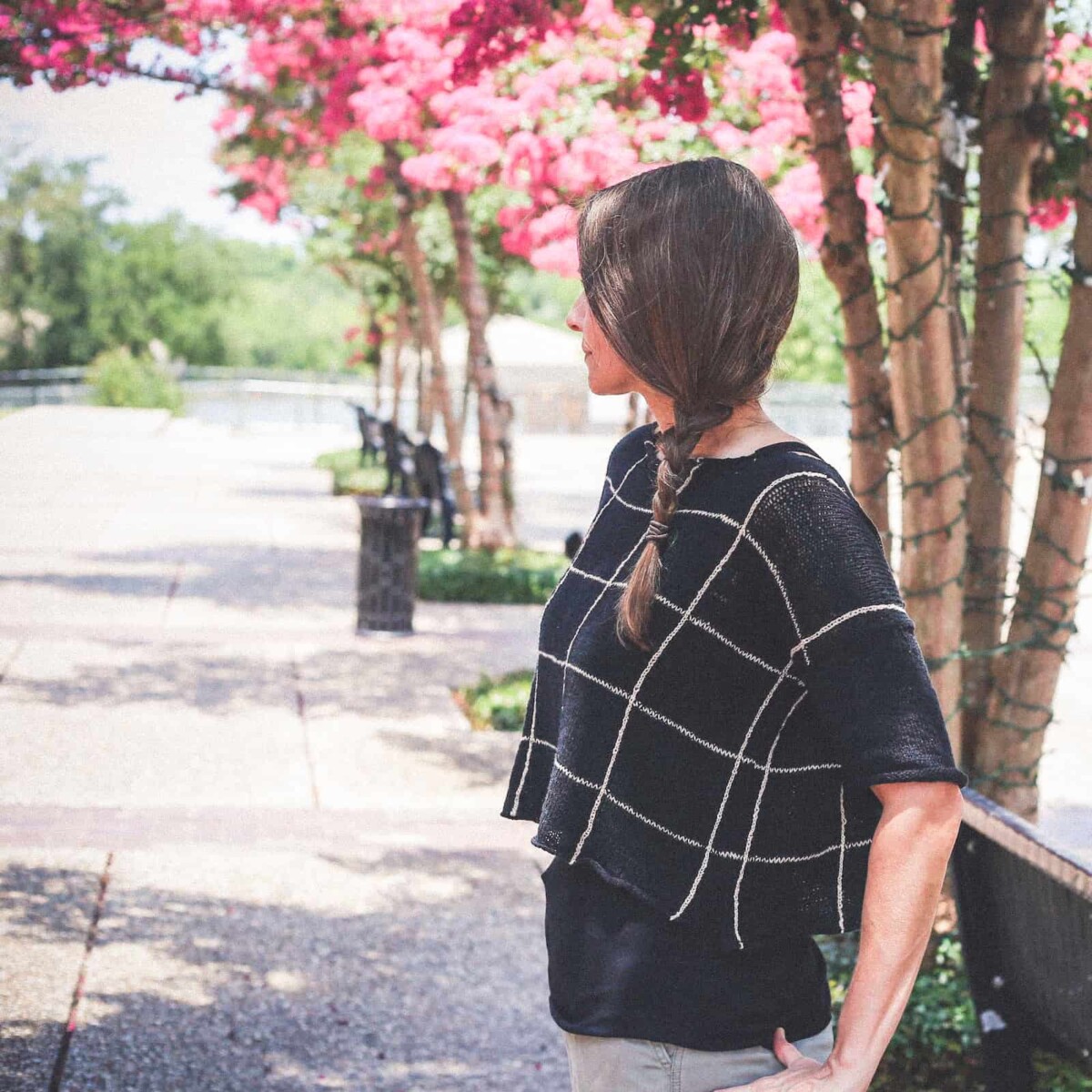 Image of me in my Zara windowpane plaid summer top standing beneath trees in bloom.